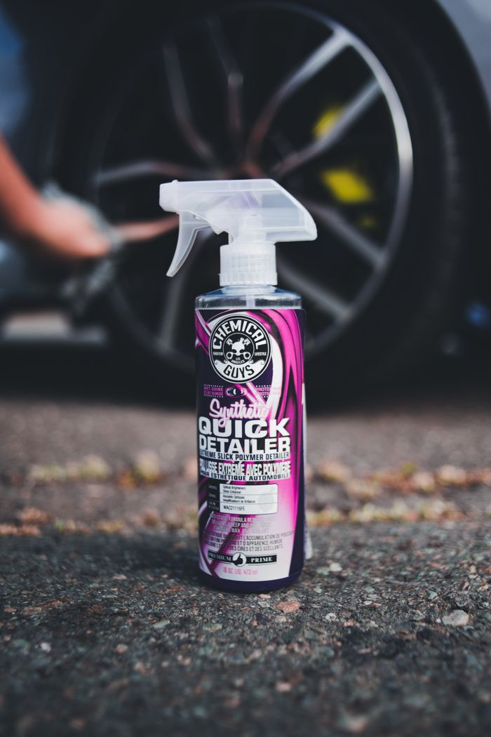 A detailed shot of a car care detailing spray bottle with a blurred car wheel in the background.