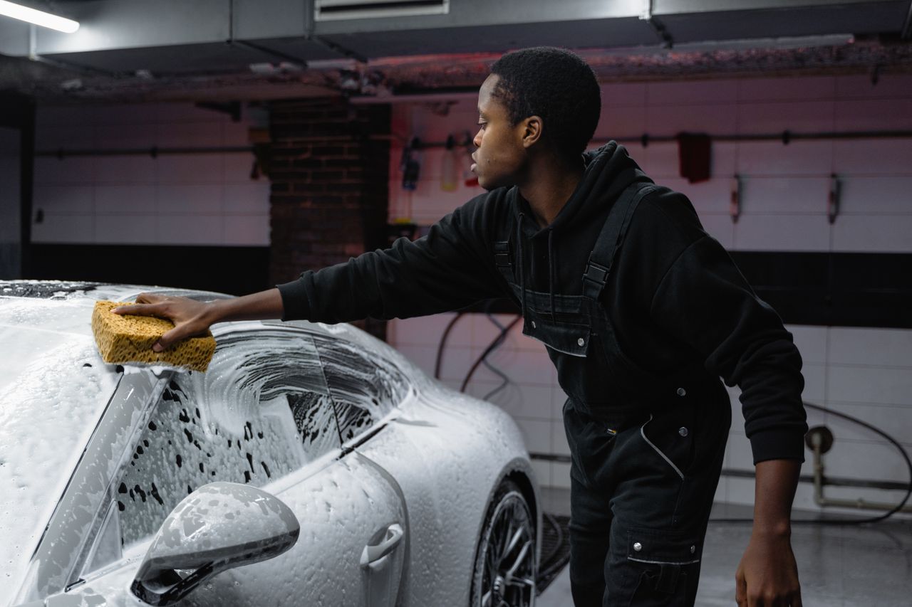 A person washing a car with a sponge, deep cleaning in a garage setting.