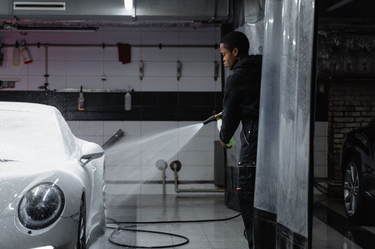 A person using a pressure washer to clean a car in an indoor garage setting.